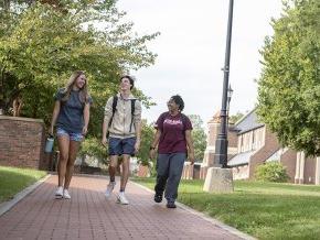 Three students walking across campus with Grace Chapel and Shaw Plaza in the background