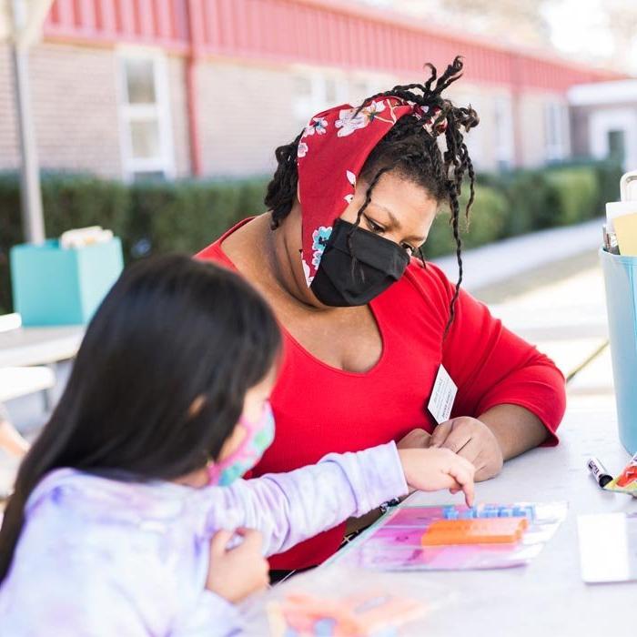 A student works with a child at an outside table